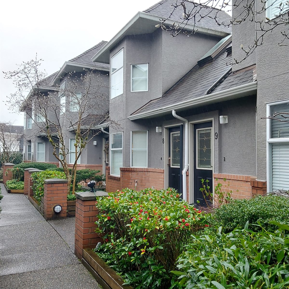 Row of grey stucco strata duplexes with landscaped entries, North Vancouver