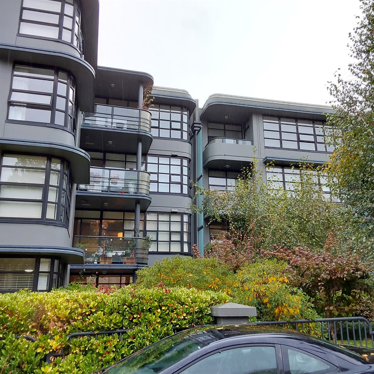 Modern low-rise residential building with curved balconies and greenery, Vancouver