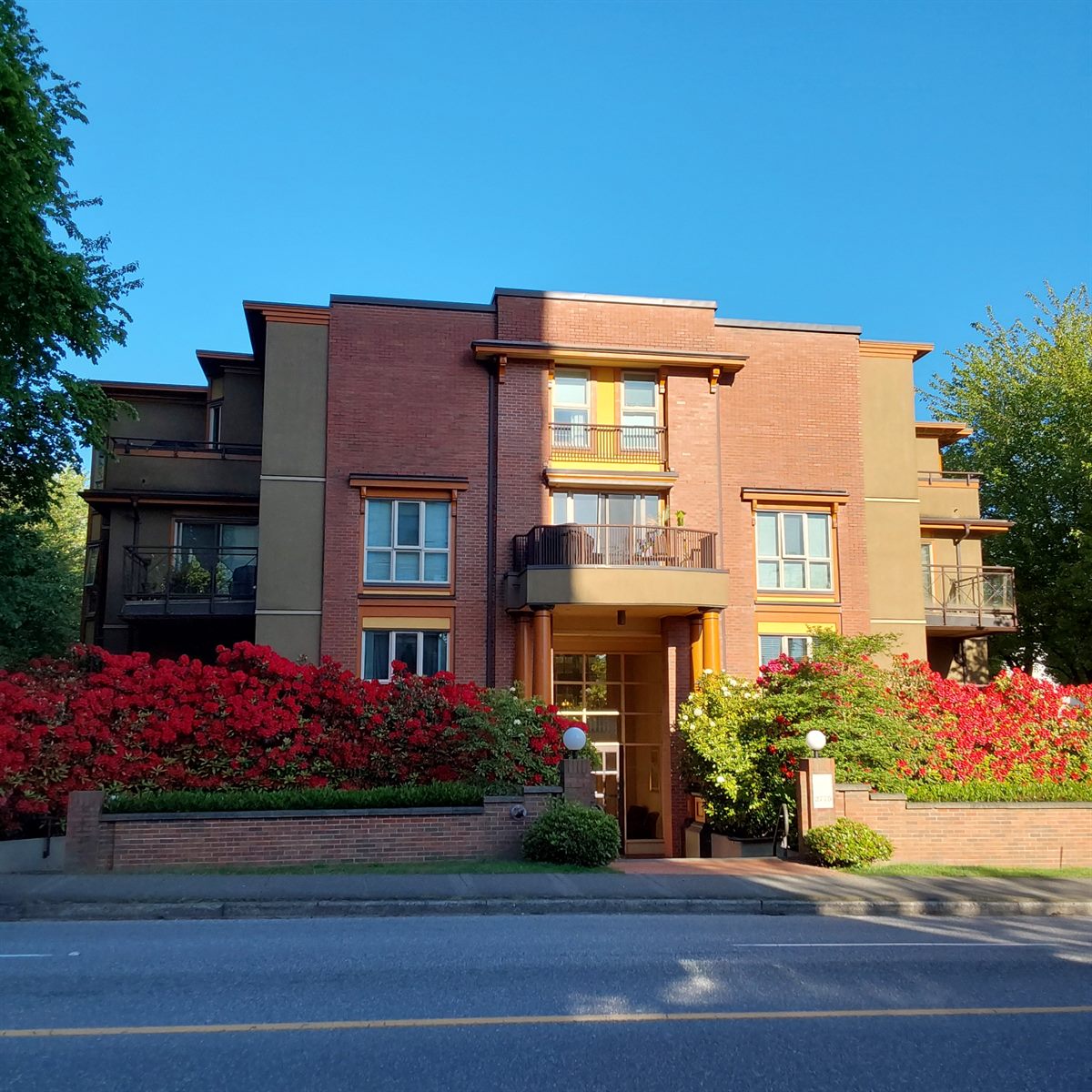Three-storey brick low-rise residential building with flowering shrubs in bloom, Vancouver