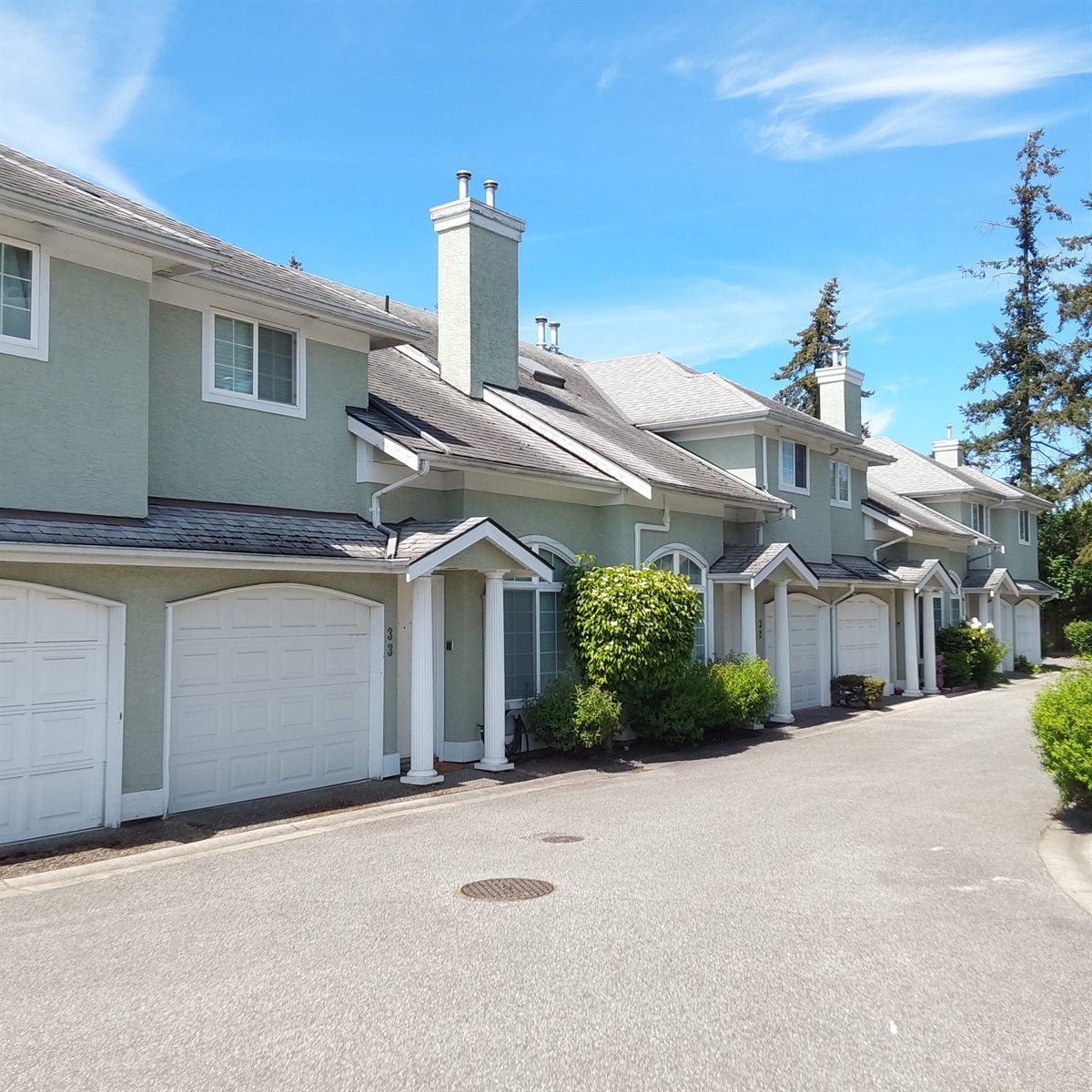 Green stucco townhome complex with private garages on a sunny day, Richmond