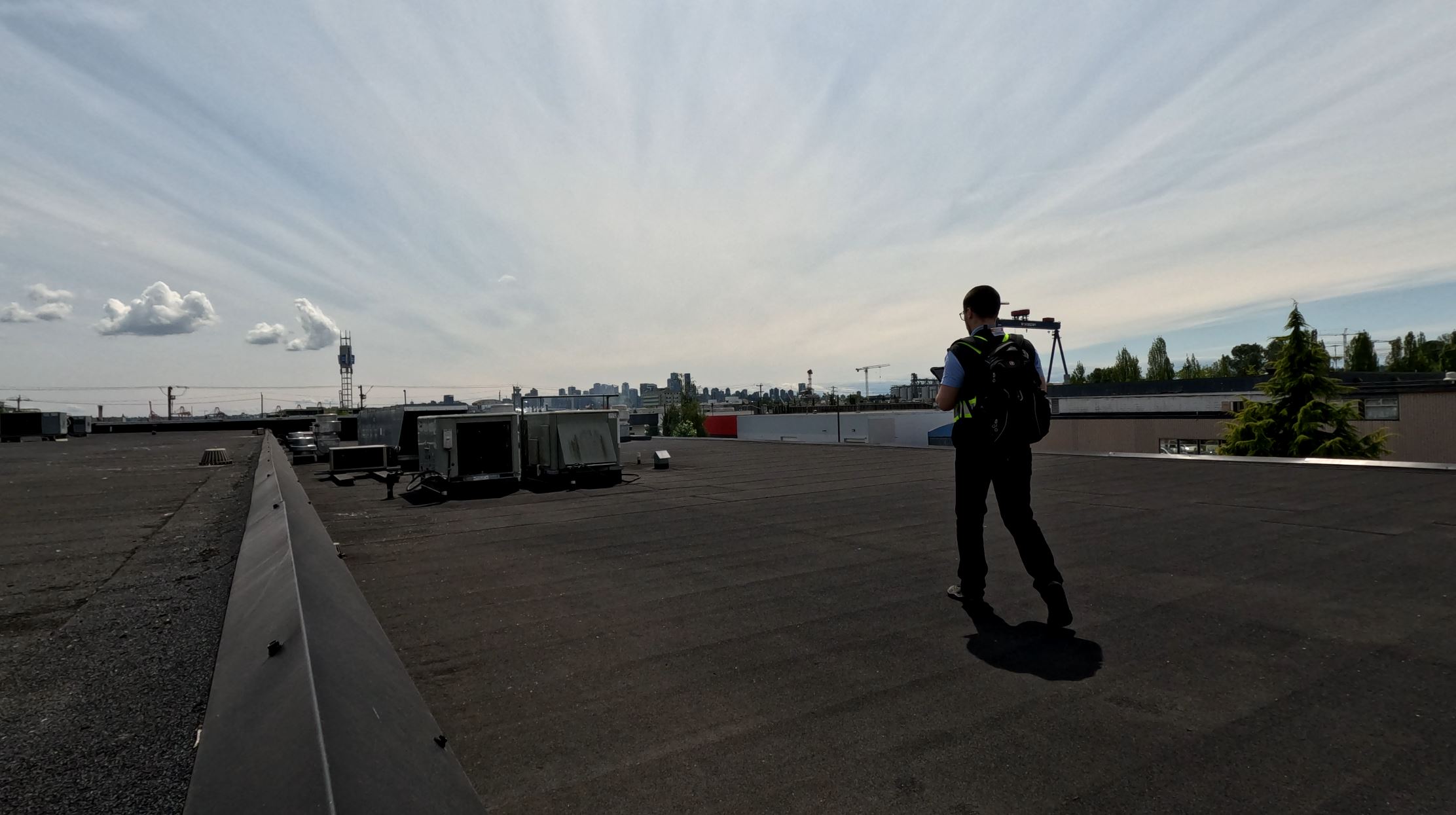 An inspector on a building's flat roof photographing rooftop mechanical units during a site inspection